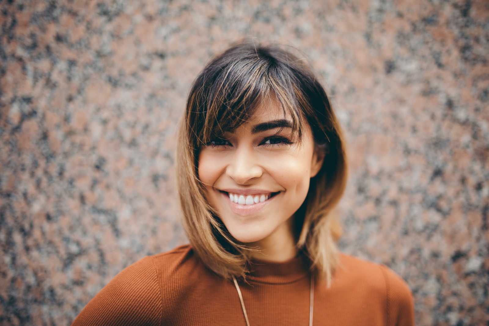 Testimonials Young woman wearing a brown sweater smiling, with orange and black pattern behind her